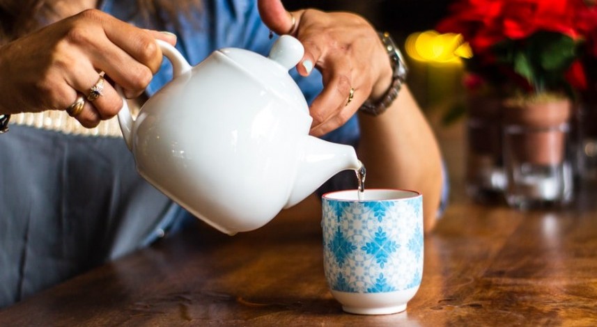 Woman pouring tea into blue and white ceramic cup on wood table.
