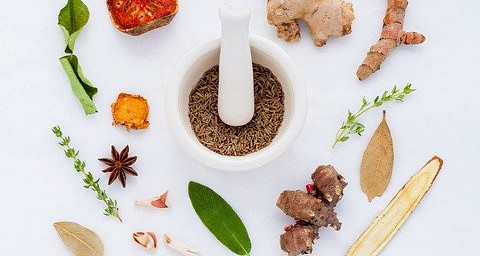 A mortar and pestle surrounded by herbs, spices and plants.